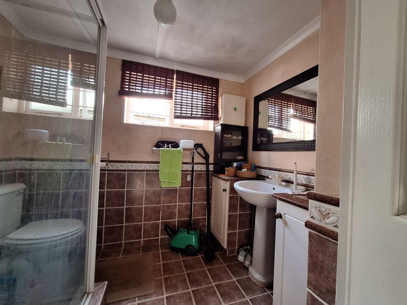 A functional bathroom featuring a pedestal basin, shower enclosure, and tiled finishes, offering potential for modernization and aesthetic updates.
