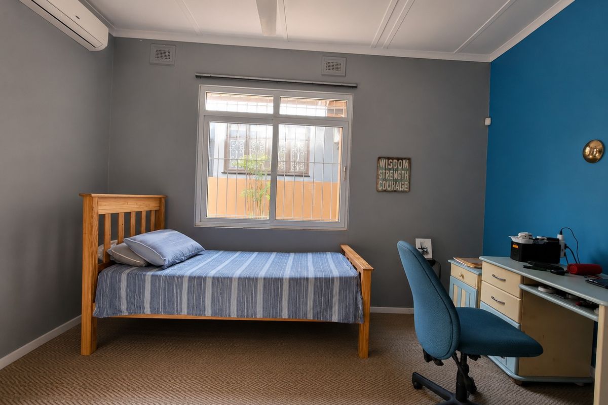 A bedroom featuring carpeted flooring, a split-system air conditioner, and a window fitted with security bars.