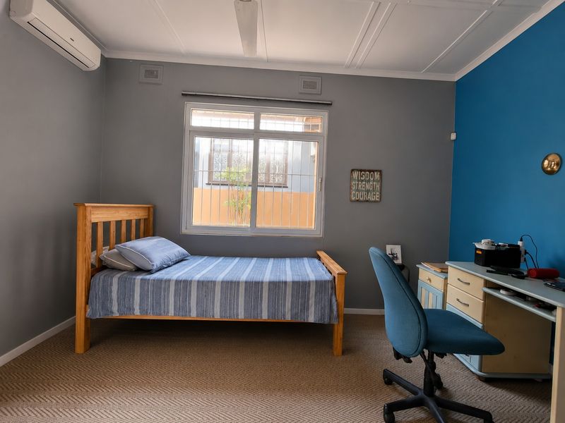 A bedroom featuring carpeted flooring, a split-system air conditioner, and a window fitted with security bars.