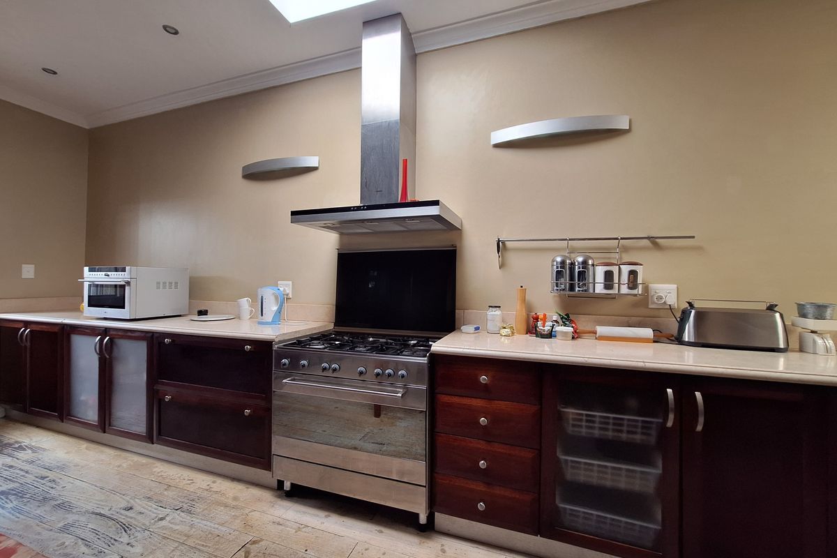 A functional kitchen featuring dark wood cabinetry, stone countertops, a stainless steel gas stove with extractor fan, and a skylight providing natural light.