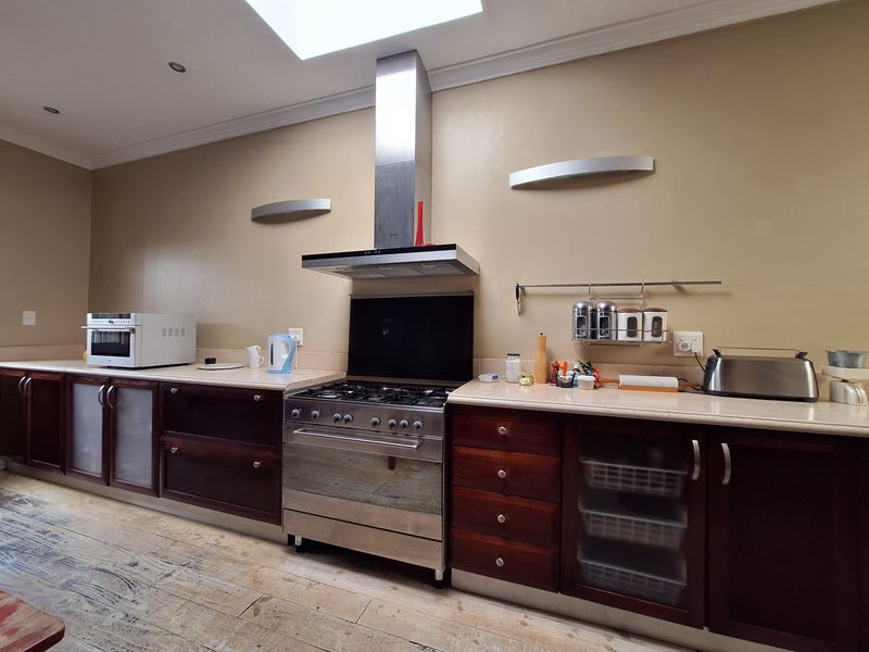 A functional kitchen featuring dark wood cabinetry, stone countertops, a stainless steel gas stove with extractor fan, and a skylight providing natural light.
