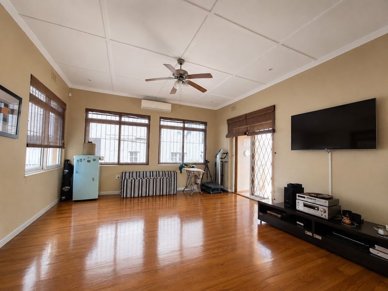 Spacious living room featuring polished hardwood flooring, a ceiling fan, and a wall-mounted air conditioning unit with access to an outdoor area.