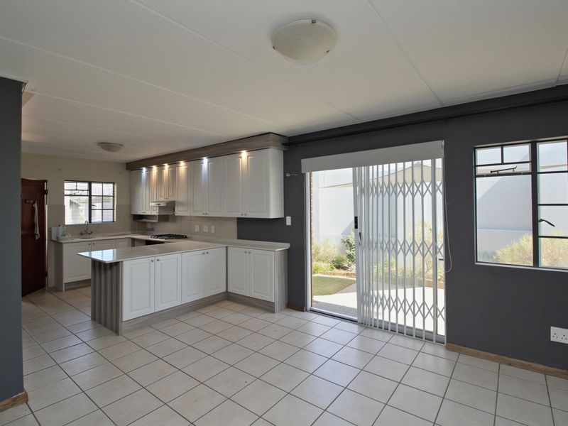 Open-plan kitchen and living area featuring white cabinetry, a central island, tiled flooring, and direct access to the rear patio through a sliding door.