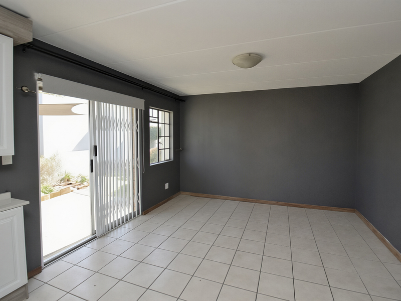 An empty open-plan living area featuring tiled floors, dark grey walls, and a sliding glass door providing access to the outdoor patio area.