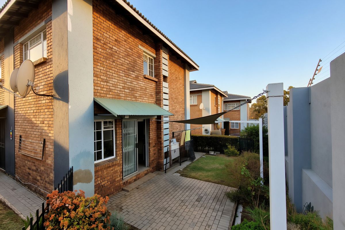 Rear view of a townhouse featuring a brick facade, paved patio area, security gate, and perimeter electric fencing.