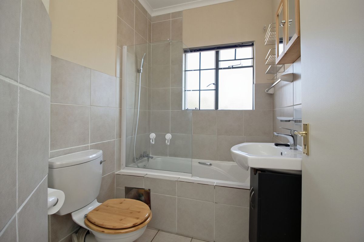 A functional bathroom featuring a bathtub with a glass shower screen, a pedestal washbasin, and neutral wall tiling.