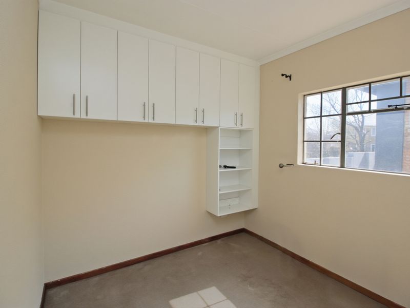A vacant bedroom featuring built-in overhead cabinetry and shelving, neutral wall finishes, and a window providing natural light.