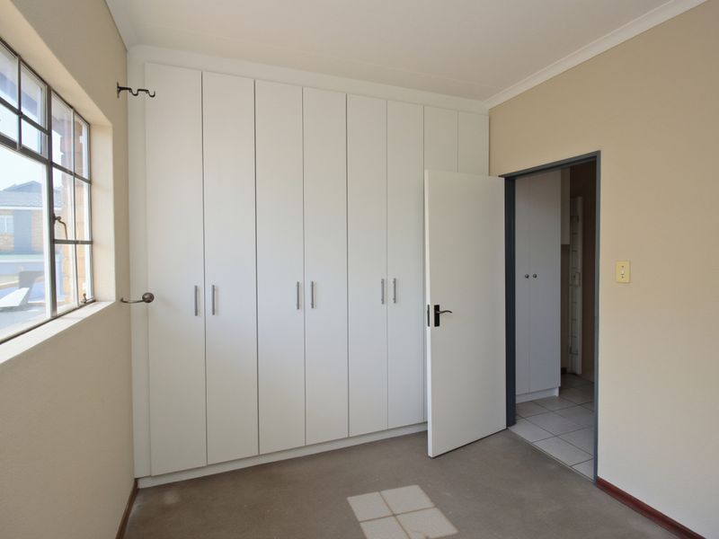 A clean, empty bedroom featuring neutral walls, carpeted flooring, and extensive built-in white cupboards, offering a versatile space ready for personalization.