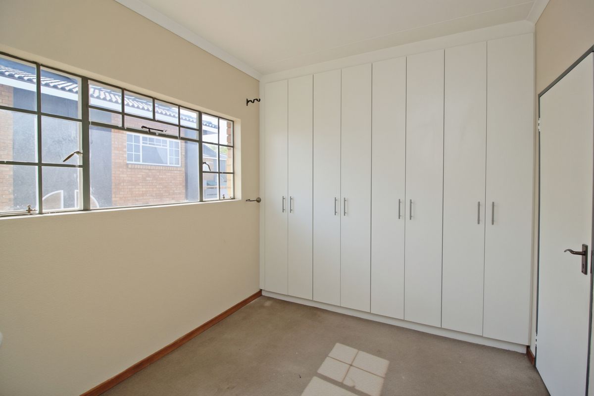 A clean, empty bedroom featuring extensive white built-in cupboards and a steel-framed window, providing a neutral canvas for personalization.
