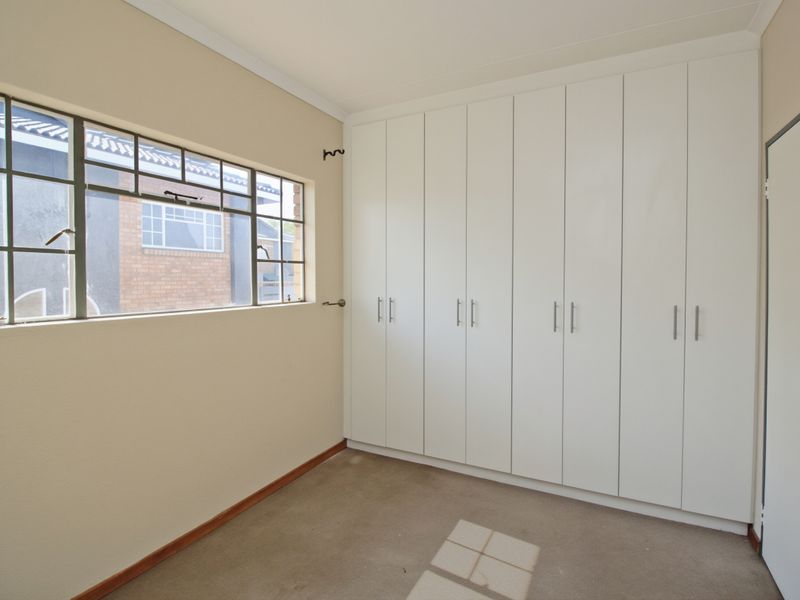 A clean, empty bedroom featuring extensive white built-in cupboards and a steel-framed window, providing a neutral canvas for personalization.