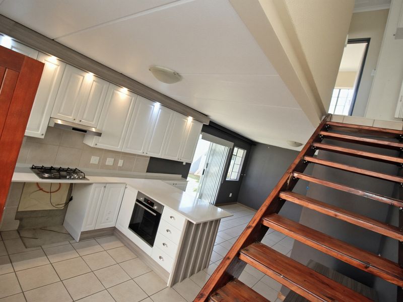 Open-plan kitchen featuring white cabinetry, stone countertops, and a gas hob, adjacent to a wooden staircase leading to the upper level.