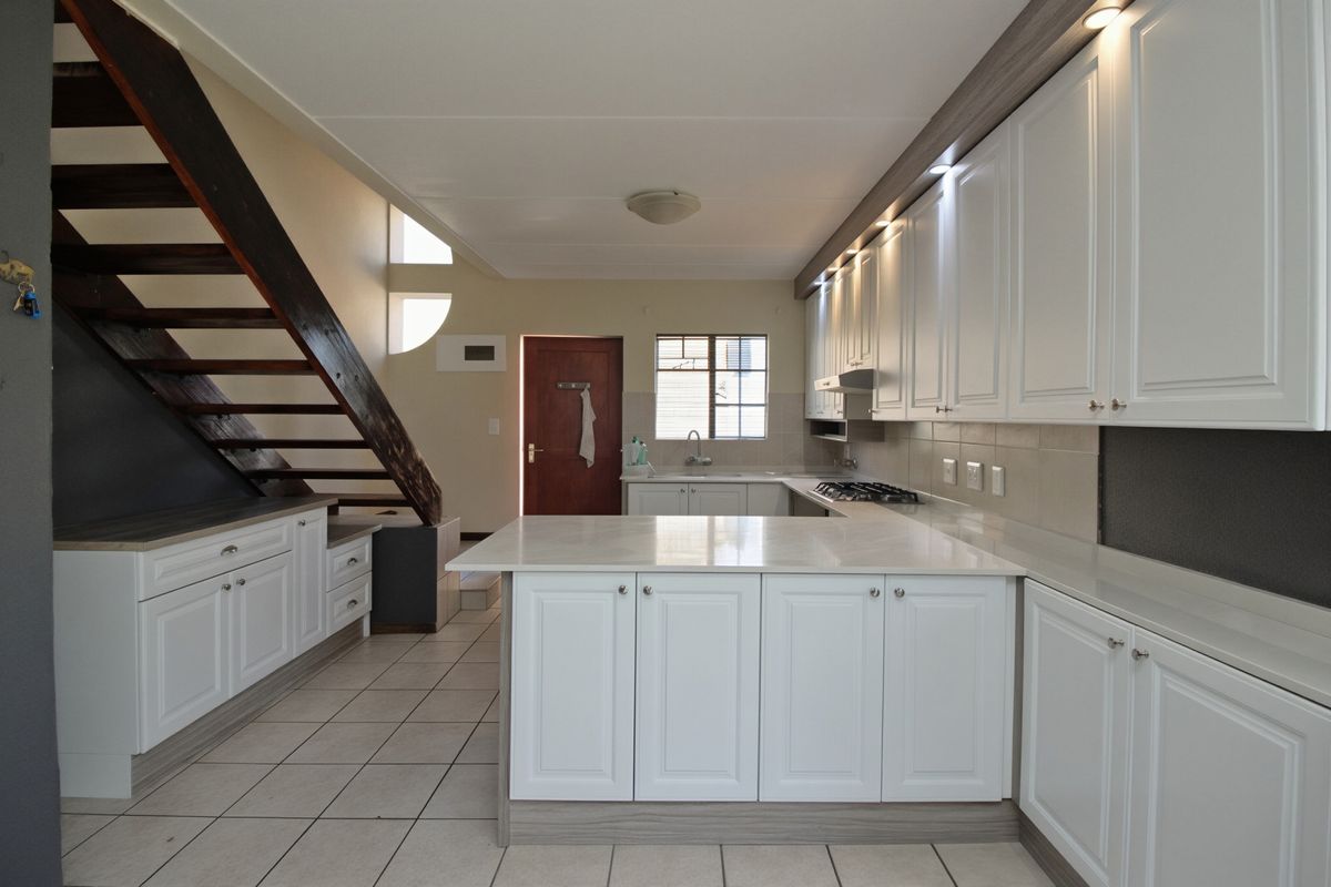 Modern kitchen featuring white cabinetry, stone countertops, gas hob, and integrated lighting, with an open-plan layout adjacent to a wooden staircase.