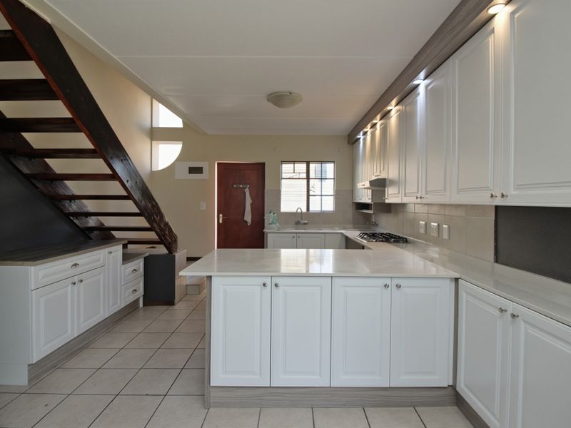 Modern kitchen featuring white cabinetry, stone countertops, gas hob, and integrated lighting, with an open-plan layout adjacent to a wooden staircase.