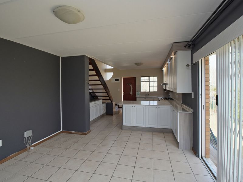 Spacious open-plan living and kitchen area featuring modern white cabinetry, a functional kitchen island, tiled flooring, and direct access to the outdoors via sliding doors.