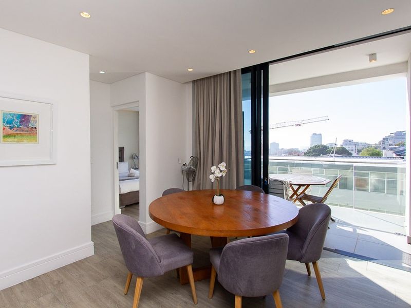 Modern open-plan dining area featuring light wood-look flooring, recessed lighting, and large sliding doors opening onto a private balcony with city views.
