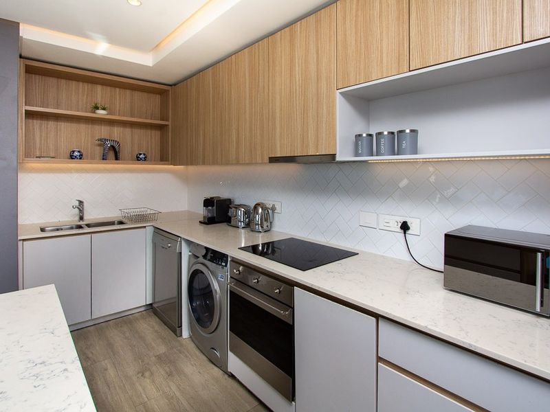 Modern kitchen featuring light wood cabinetry, stone countertops, herringbone tile backsplash, integrated appliances, and recessed ceiling lighting.