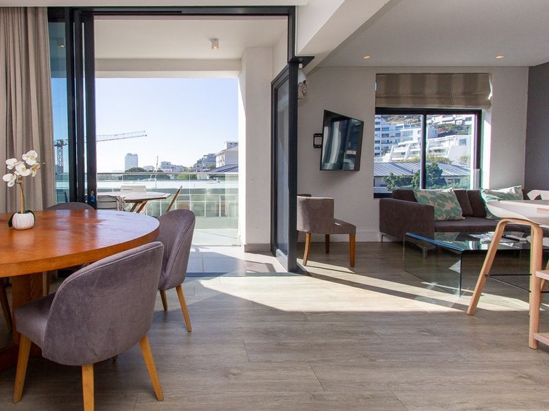 Bright open-plan living and dining area featuring modern laminate flooring, recessed lighting, and seamless access to a private balcony through large bi-fold doors.