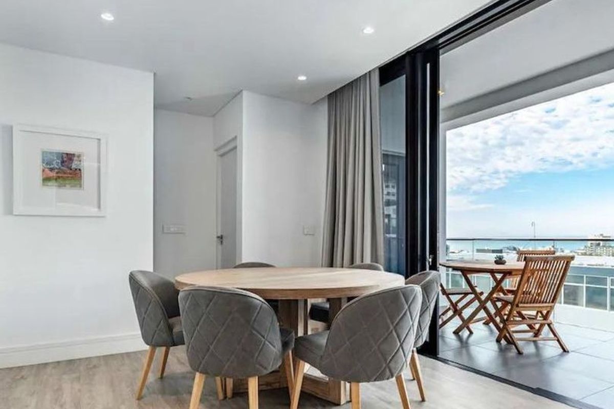 Modern open-plan dining area featuring light laminate flooring, recessed lighting, and seamless access to a spacious balcony with scenic views through large sliding doors.