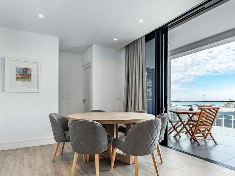 Modern open-plan dining area featuring light laminate flooring, recessed lighting, and seamless access to a spacious balcony with scenic views through large sliding doors.