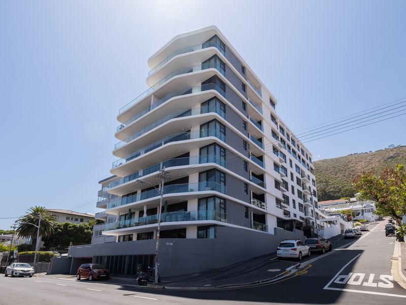Modern multi-story apartment building featuring contemporary architectural design, extensive glass balconies, and street-level parking access in a prime urban location.