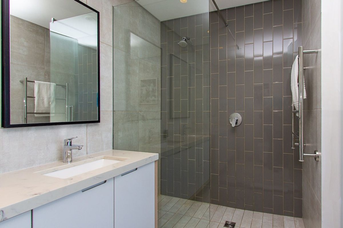 Modern bathroom featuring a stone-topped vanity, walk-in shower with glass screen, and contemporary wall tiling with a heated towel rail.