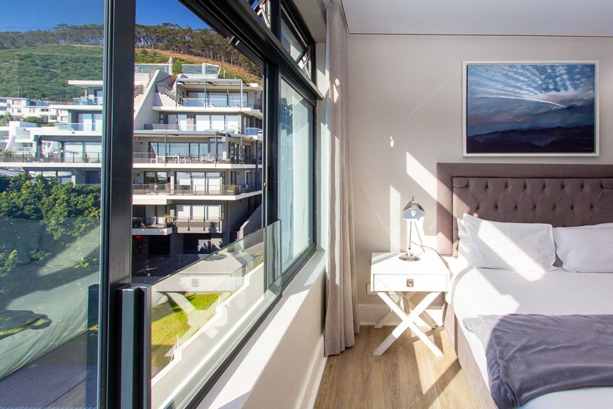 A bright, modern bedroom featuring large aluminium-framed windows that offer an expansive view of the surrounding residential complex.