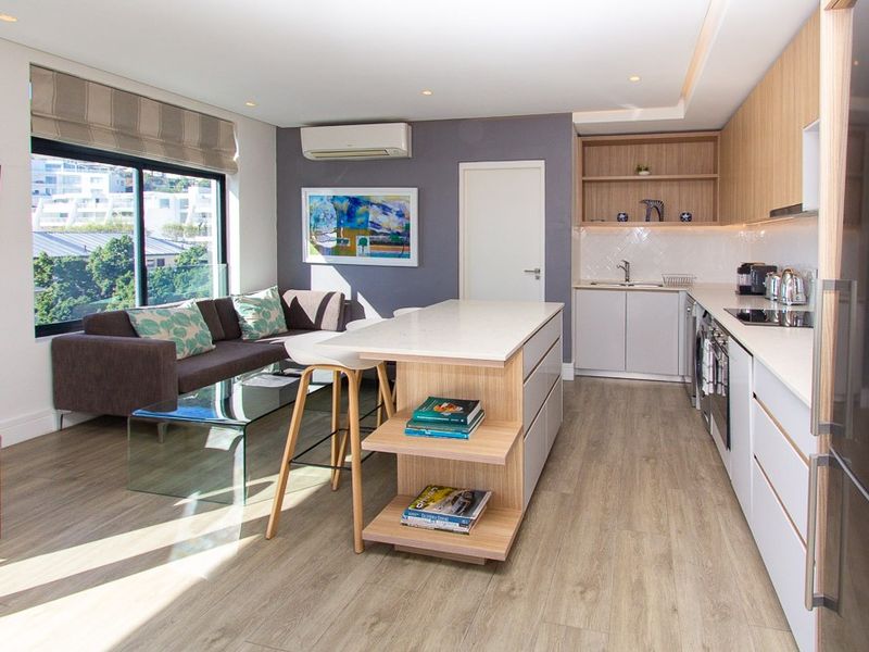 Modern open-plan living area featuring a sleek kitchen with stone countertops, integrated appliances, and a central island, flowing into a bright, air-conditioned lounge space.