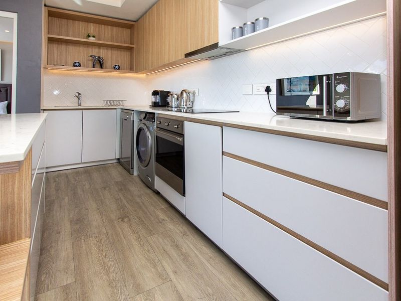 Modern kitchen featuring sleek cabinetry, stone countertops, integrated appliances, and stylish herringbone tile backsplash with warm under-cabinet lighting.