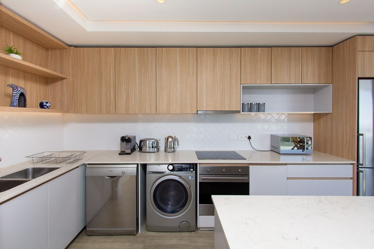 Modern kitchen featuring light wood cabinetry, stone countertops, herringbone tile backsplash, and integrated appliances including an oven and cooktop.
