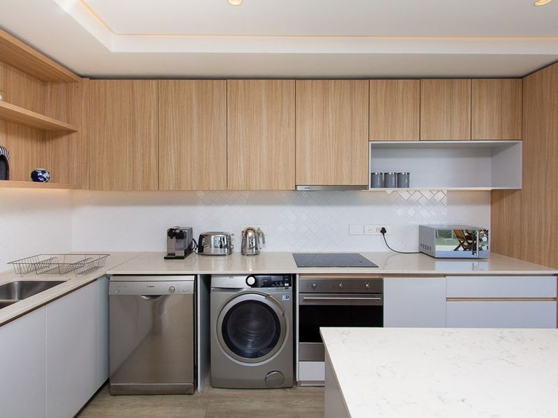 Modern kitchen featuring light wood cabinetry, stone countertops, herringbone tile backsplash, and integrated appliances including an oven and cooktop.