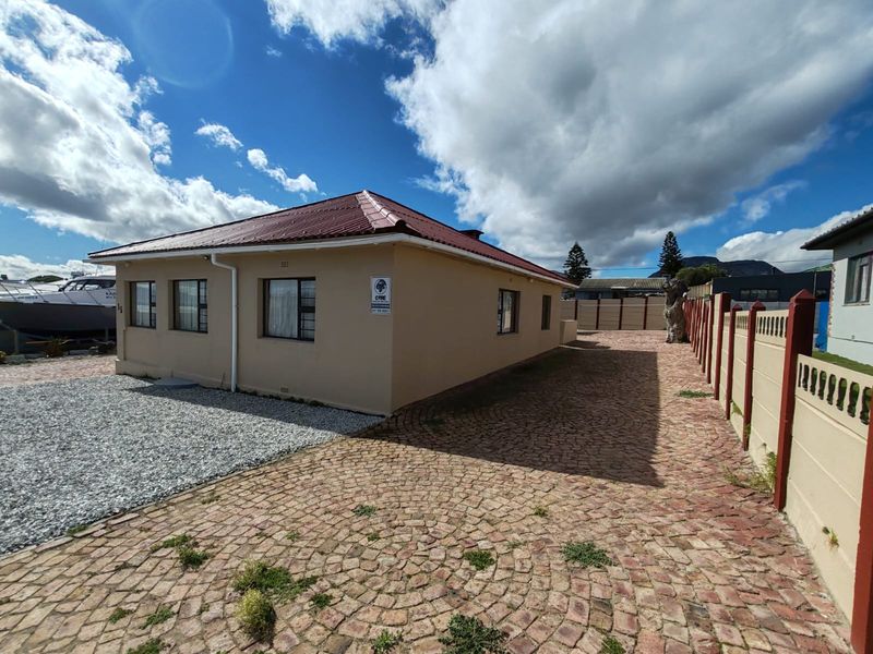 Exterior view of a single-story house featuring a corrugated metal roof, paved driveway, and secure perimeter walling.