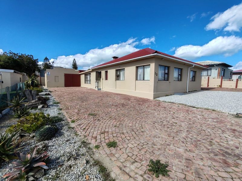 Front exterior view of a single-story house featuring a red metal roof, cobblestone driveway, and secure boundary walling.