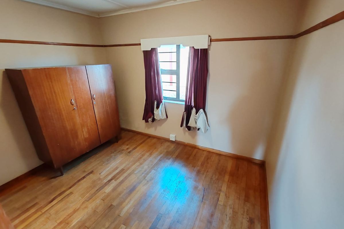 A bedroom featuring original hardwood flooring, a picture rail, and a window fitted with security bars.