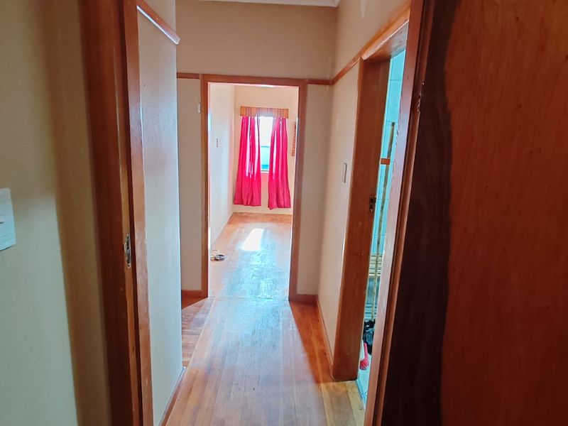 A narrow hallway featuring original timber flooring and classic timber door frames, leading through to an adjacent room.
