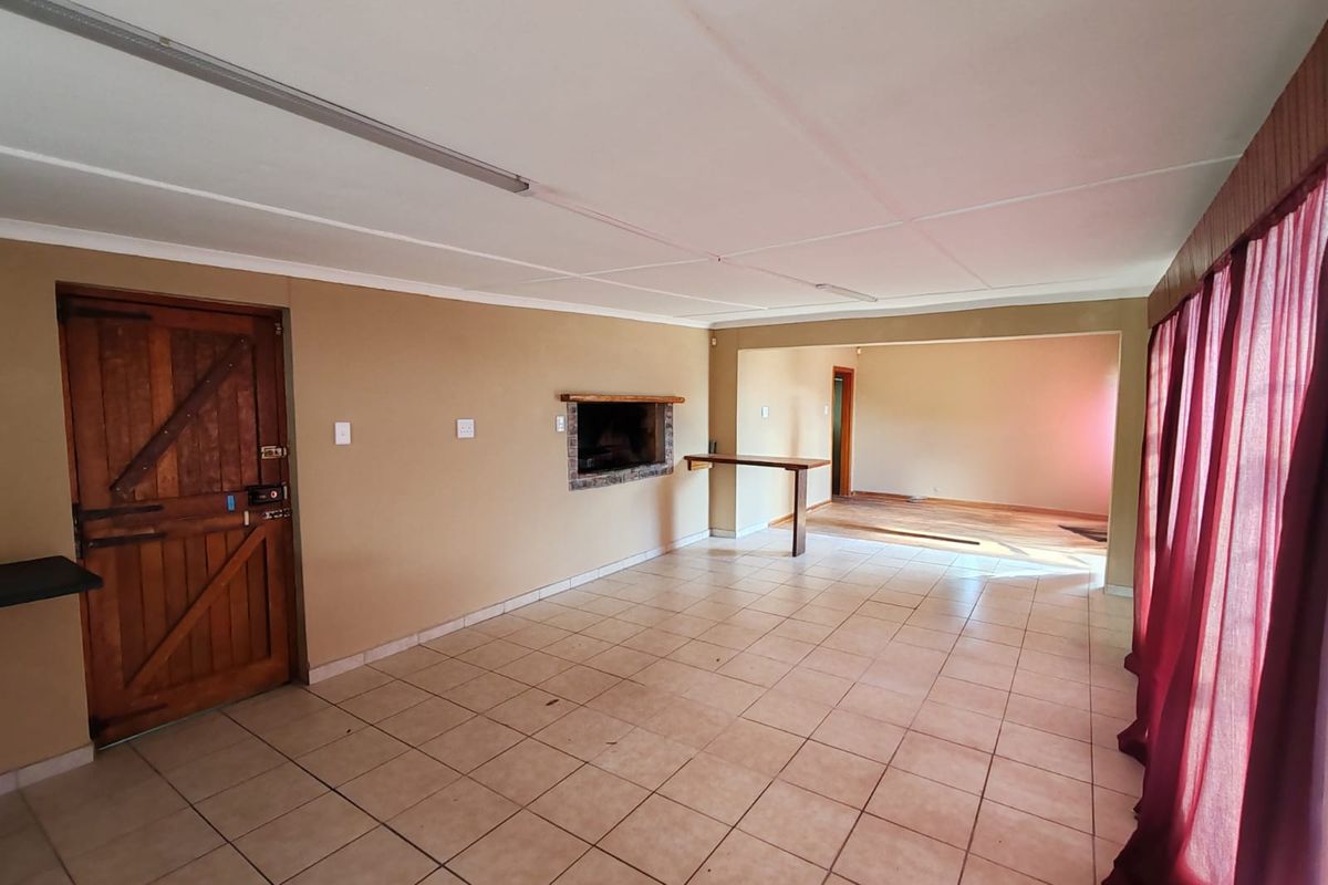 Spacious living area featuring tiled flooring, a built-in fireplace, and a rustic timber door, offering a versatile layout for modern interior design.