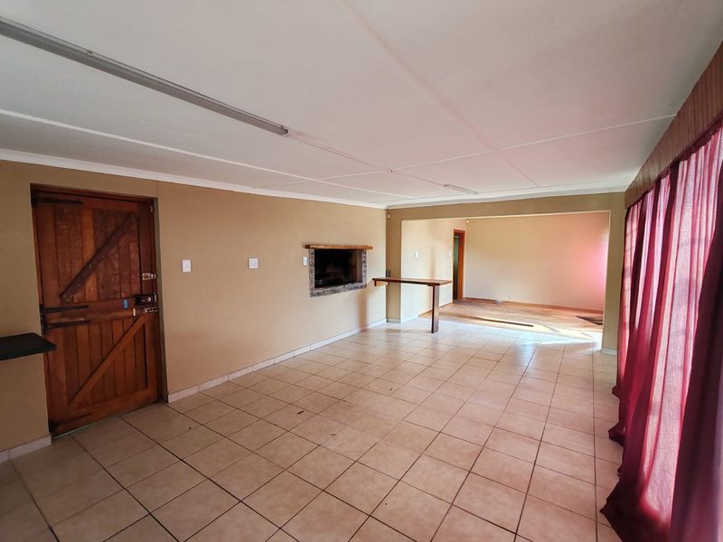 Spacious living area featuring tiled flooring, a built-in fireplace, and a rustic timber door, offering a versatile layout for modern interior design.