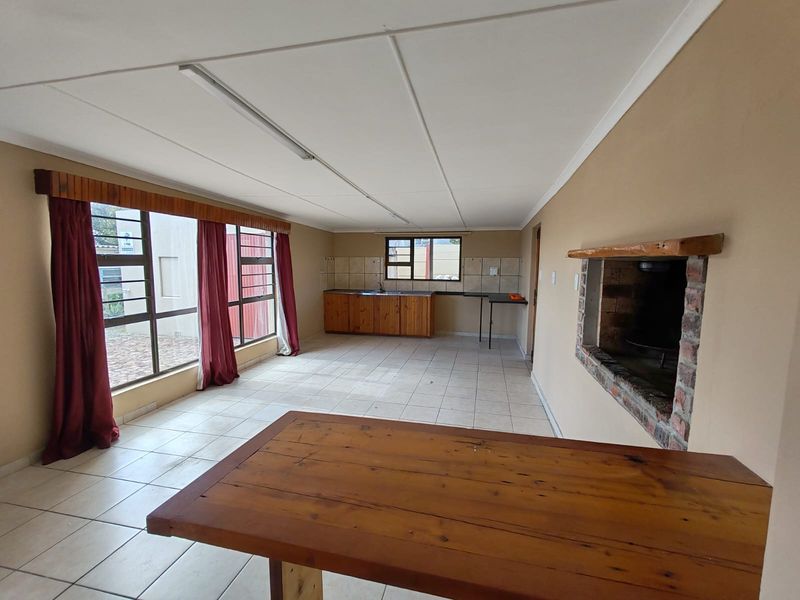 Open-plan living and kitchen area featuring tiled floors, a built-in brick fireplace, and functional wooden cabinetry with ample natural light.