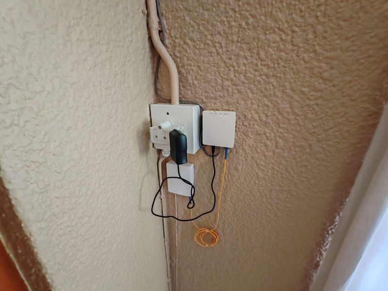 A utility corner featuring a wall-mounted fiber optic terminal and electrical power point with exposed cabling.