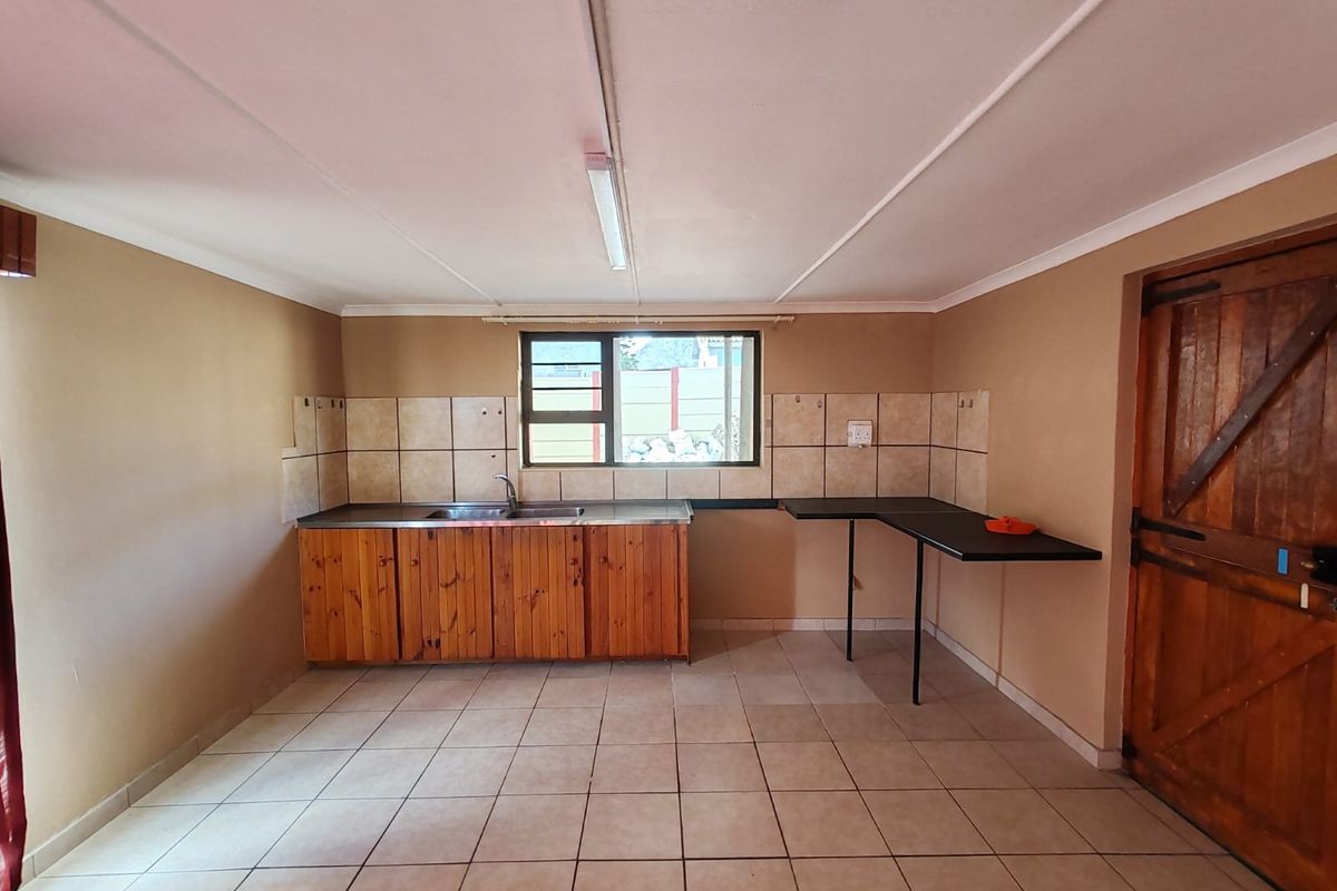 A functional, empty kitchen space featuring wooden cabinetry, a stainless steel sink, tiled backsplash, and tiled flooring, ready for a modern update.