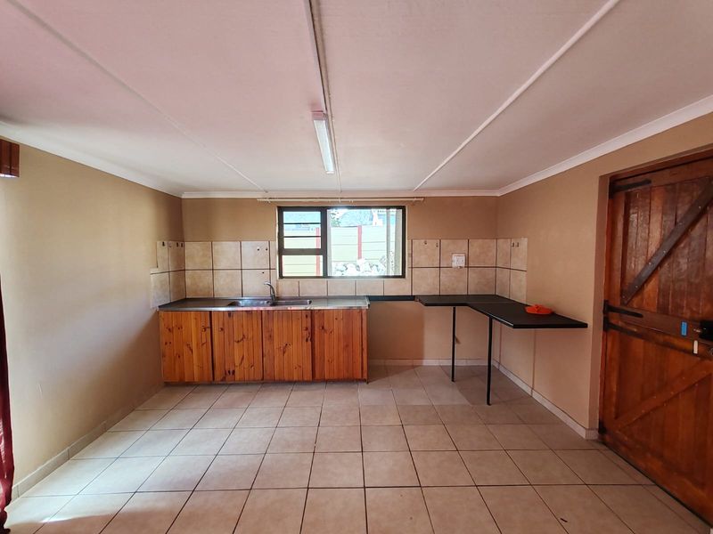 A functional, empty kitchen space featuring wooden cabinetry, a stainless steel sink, tiled backsplash, and tiled flooring, ready for a modern update.