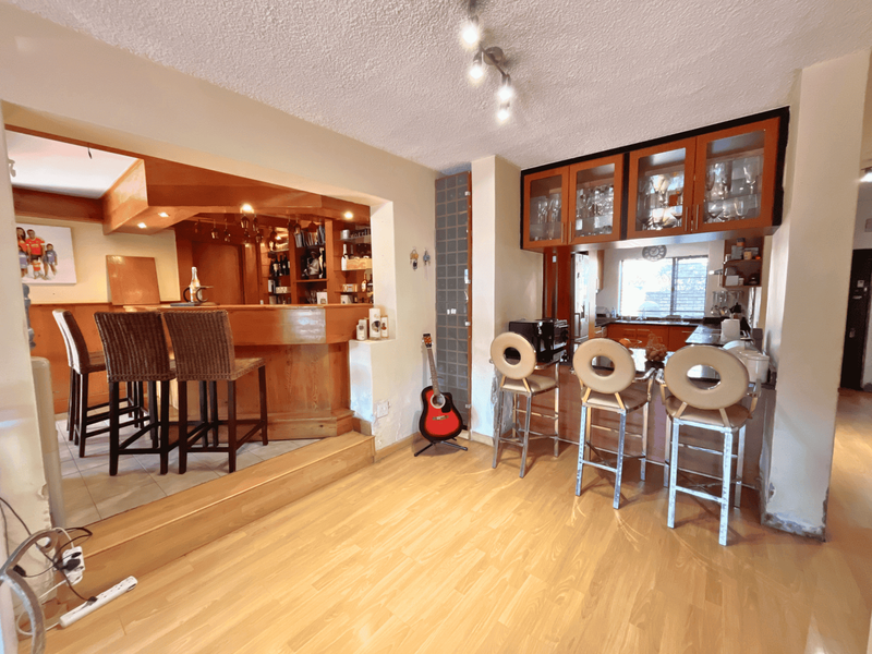 Open plan living area featuring a raised built-in bar section and a functional kitchen with overhead cabinetry and laminate flooring throughout.