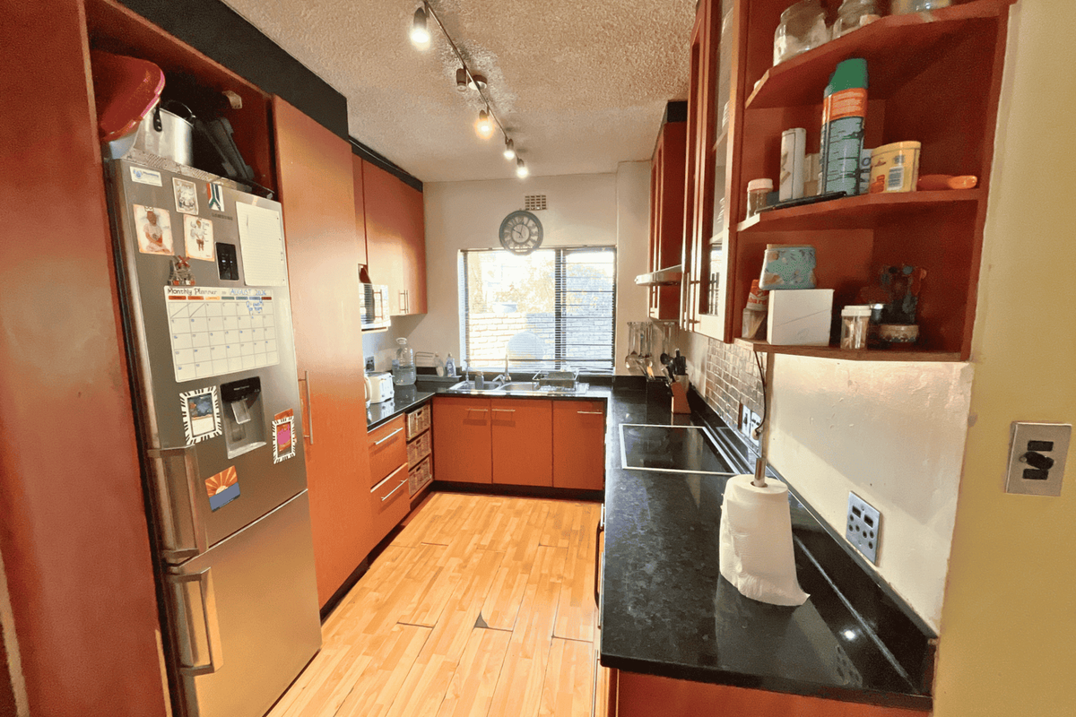 A functional galley-style kitchen featuring dark granite countertops, built-in wooden cabinetry, an electric hob, and track lighting.