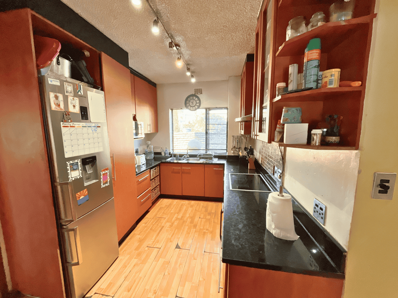 A functional galley-style kitchen featuring dark granite countertops, built-in wooden cabinetry, an electric hob, and track lighting.