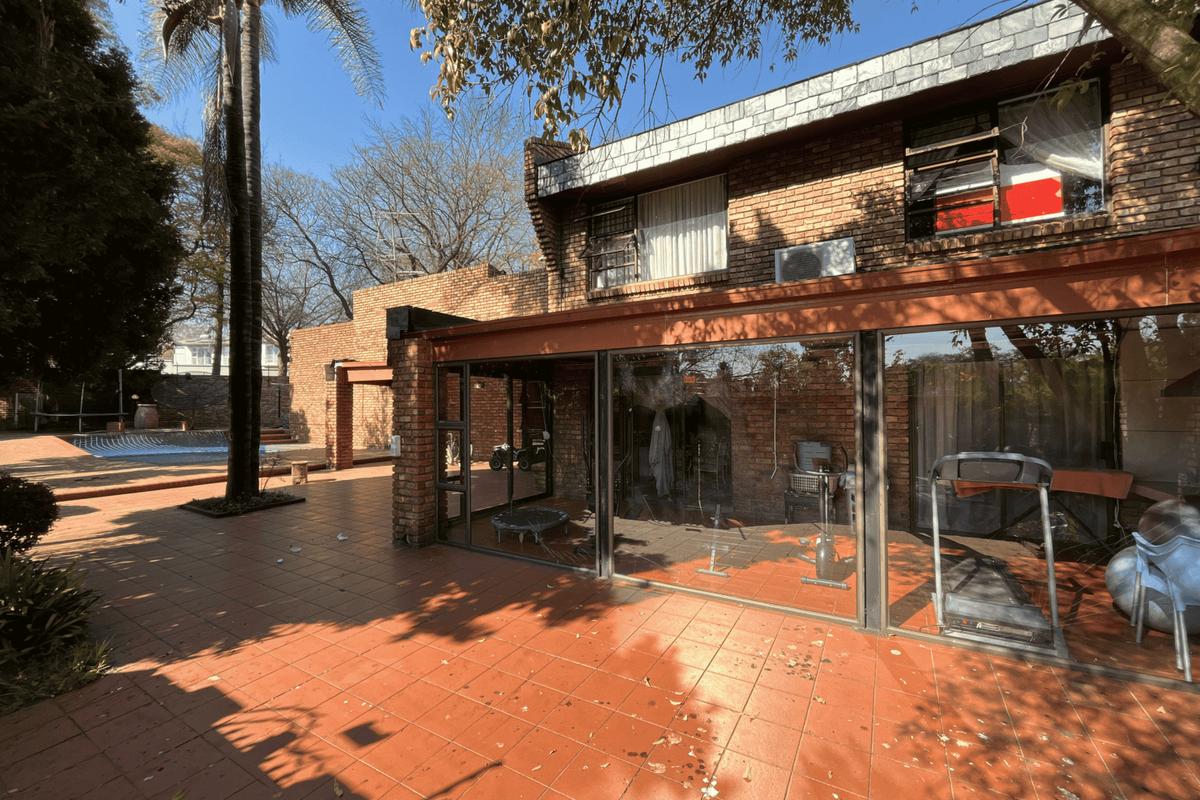 Rear exterior view of a townhouse featuring a brick facade, tiled patio area, and a swimming pool with large sliding glass doors.