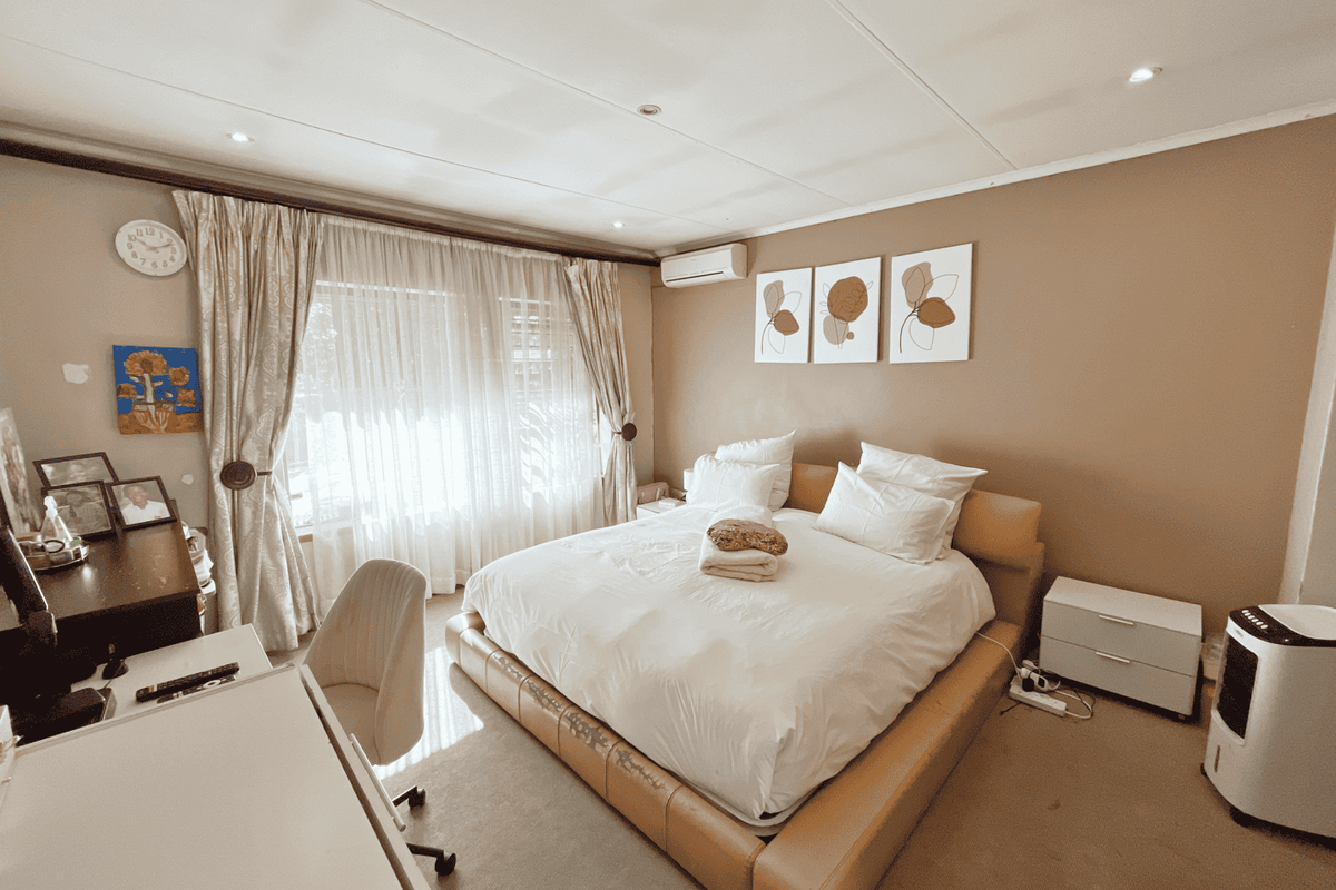 A spacious bedroom featuring neutral wall tones, recessed ceiling lighting, and a wall-mounted air conditioning unit, providing a comfortable and functional living space.