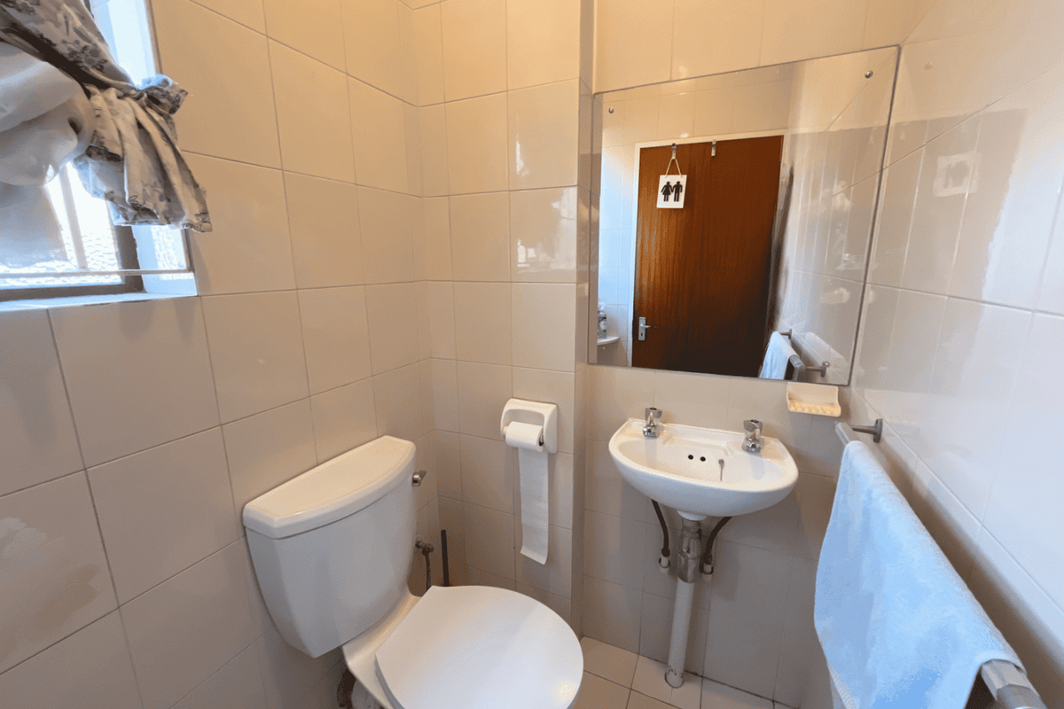A compact guest bathroom featuring a pedestal basin, toilet, and neutral wall tiling, providing a functional and clean space.