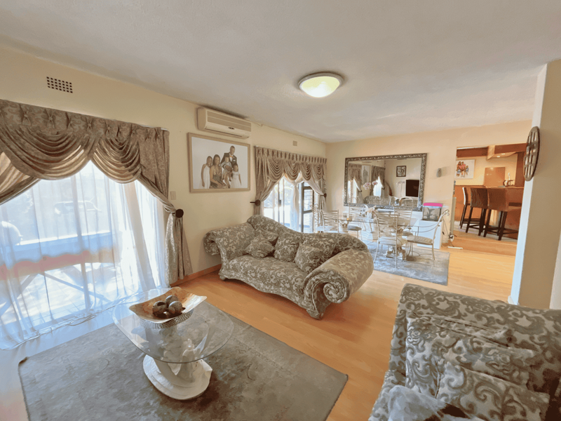 Spacious open-plan living and dining area featuring laminate flooring, air conditioning, and large sliding glass doors providing access to the outdoor space.