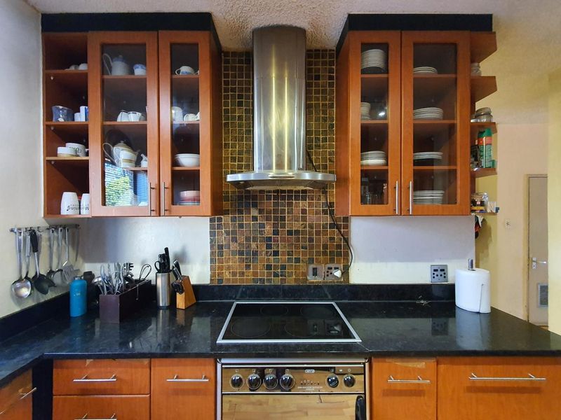 A functional kitchen featuring wooden cabinetry, a black granite countertop, mosaic tile backsplash, and a stainless steel extractor fan with a built-in electric oven.