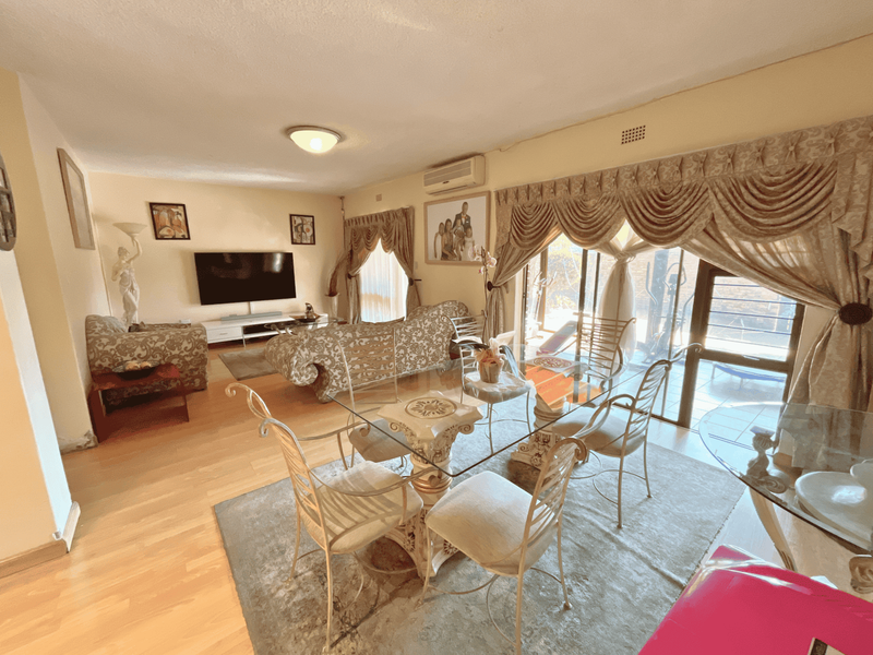 Open-plan living and dining area featuring laminate flooring, split-system air conditioning, and large sliding glass doors providing access to the outdoor space.
