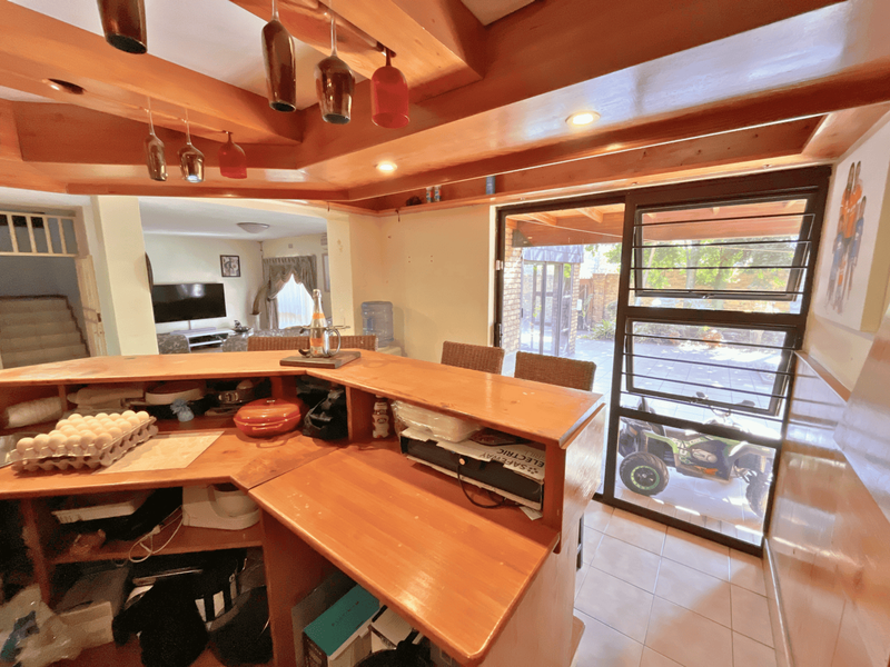 A built-in wooden bar area featuring timber ceiling beams, recessed lighting, and direct access to the outdoor patio through a sliding glass door.